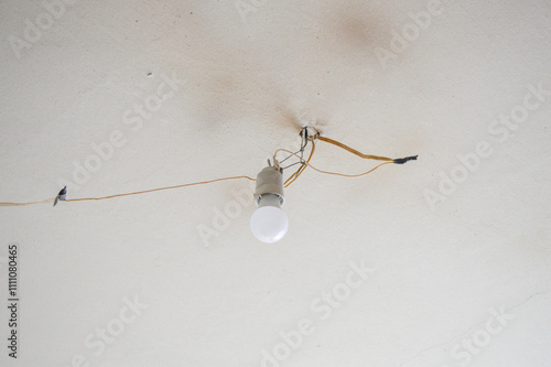exposed lightbulb fixture hanging from ceiling connected by exposed somewhat precarious wiring home repair DIY safely fixing upgrading electrical fixtures professional installation minimalism 