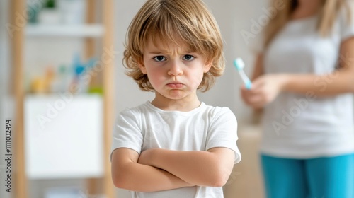 Upset child crossing arms while standing in a bathroom with a parent holding a toothbrush in the background