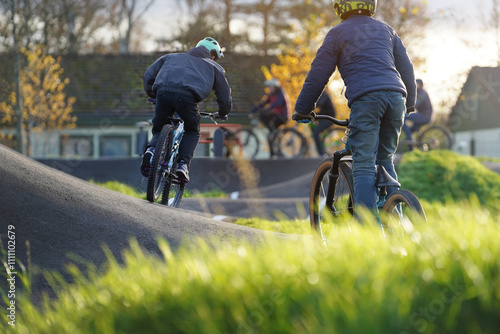 Group of kids and teens cycling on a pumptrack, enjoying an active lifestyle, bonding in nature. promoting inclusivity and fitness in a family-friendly outdoor setting during a sunny autumn day