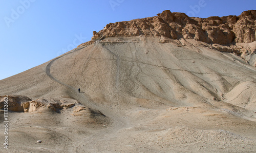 Tourist in hiking trail to a top of Mount Zin or Har Zin in Har Hahar nature reserve in Negev Desert. A steep, dust path to a top. Unique landscape of the mount, sloped sides and a top like flat table photo