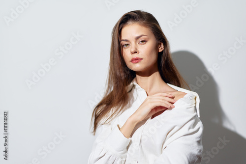 Portrait of a young woman with long hair wearing a white shirt against a light background, conveying elegance and tranquility, highlighting beauty and simplicity