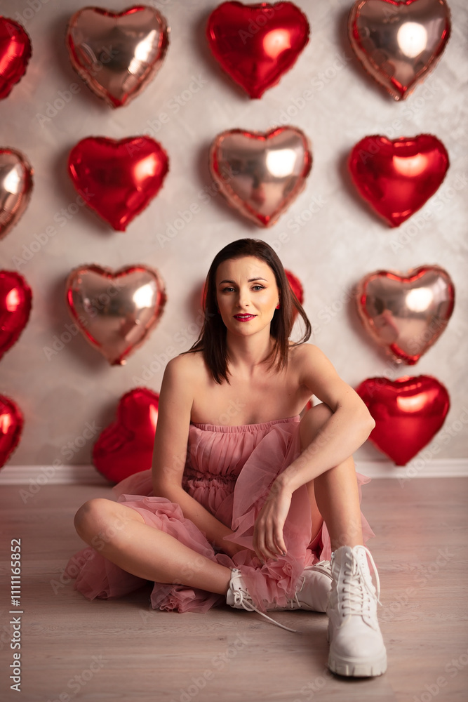 Woman in a pink ruffled dress and white boots sitting on the floor with heart-shaped balloons in the background Woman in a pink ruffled dress and white boots sitting on the floor with heart-shaped balloons in the background