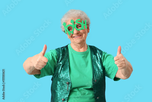 Happy senior woman in glasses and vest for St. Patrick's Day celebration showing thumbs-up on blue background photo