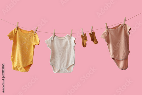 Different baby clothes and socks hanging on rope against pink background