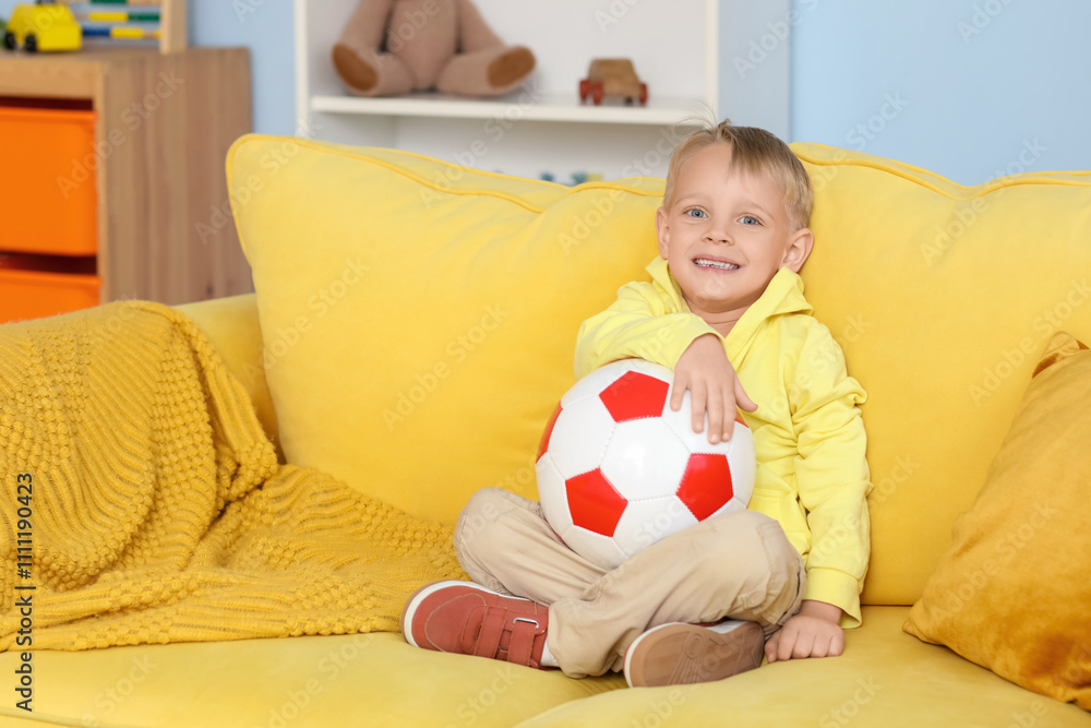 Cute little boy sitting on yellow sofa with soccer ball Cute little boy sitting on yellow sofa with soccer ball