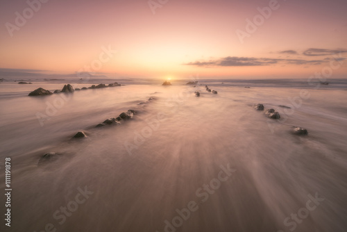 Sunset on Barrika beach, Bizkaia with the waves of the Cantabrian Sea breaking between the rocks photo