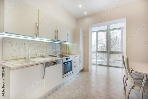 Light pink interior of a spacious kitchen with furniture and access to a glazed loggia.