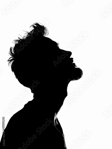 Man with a beard and short hair is standing in front of a white background. The man is looking up, and his head is tilted to the side. Concept of introspection and contemplation