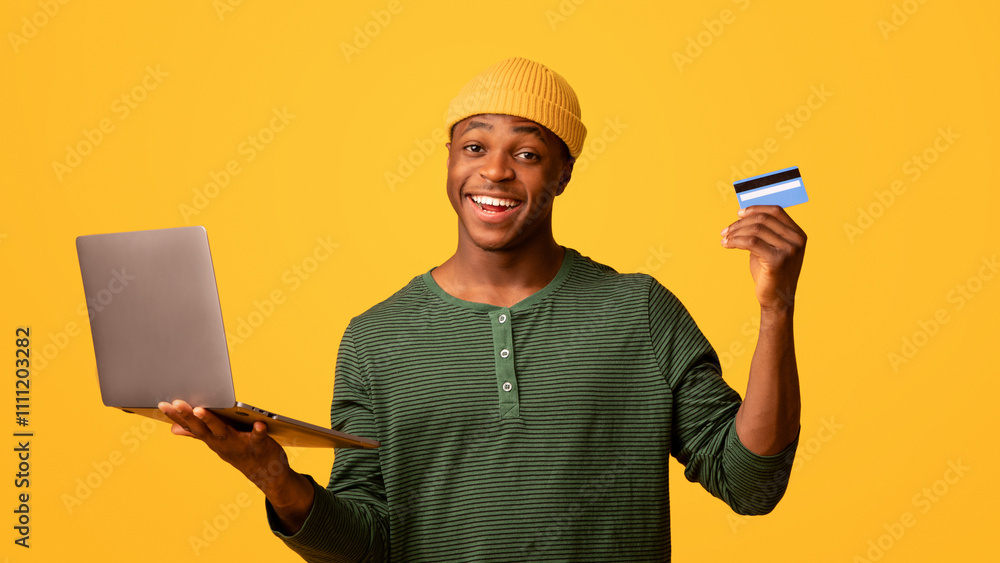 Online Shopping. Cheerful black guy with laptop and credit card posing over yellow studio background, joyful young african american man enjoying internet purchases and easy payments, copy space Online Shopping. Cheerful black guy with laptop and credit card posing over yellow studio background, joyful young african american man enjoying internet purchases and easy payments, copy space