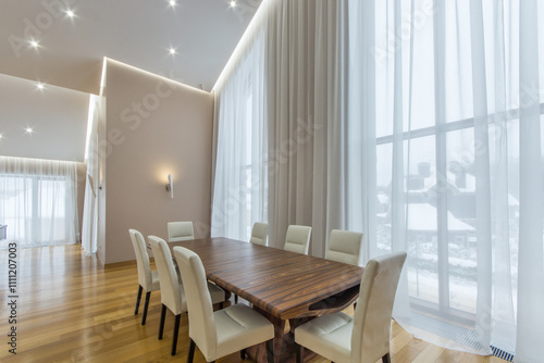 Spacious bright living room with panoramic windows, parquet floor. A long table with white chairs.