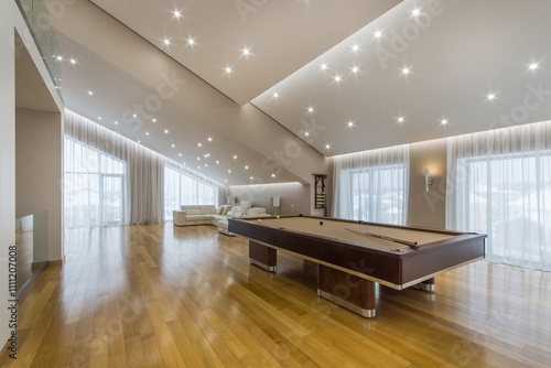 An interesting design of the living room of a private house with large windows, parquet floors and a billiard table in the center.