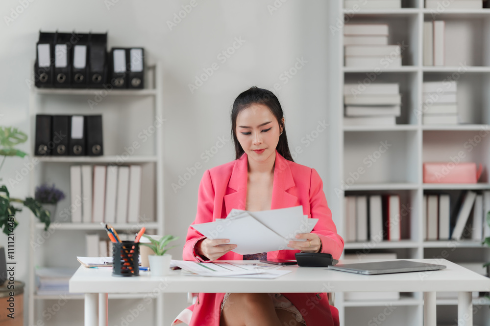 Focused Professional: A young businesswoman in a pink blazer sits at her desk, attentively reviewing documents. Her serious expression and focused gaze convey determination and dedication. Focused Professional: A young businesswoman in a pink blazer sits at her desk, attentively reviewing documents. Her serious expression and focused gaze convey determination and dedication.