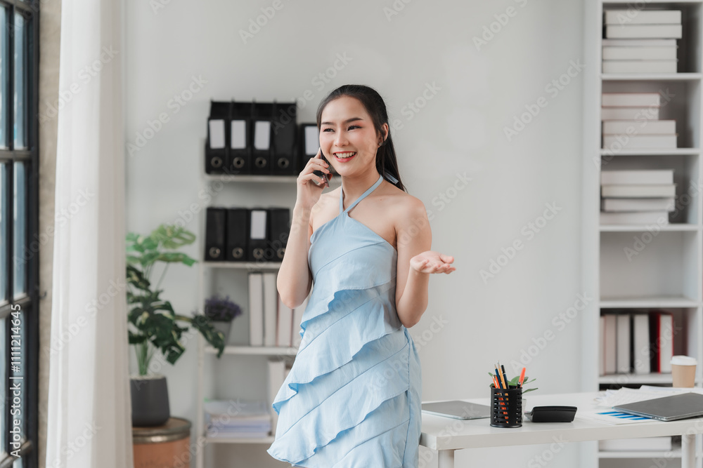 Confident and Connected: A young businesswoman in a stylish blue dress exudes confidence as she takes a call in her modern office. The bright. Confident and Connected: A young businesswoman in a stylish blue dress exudes confidence as she takes a call in her modern office. The bright.