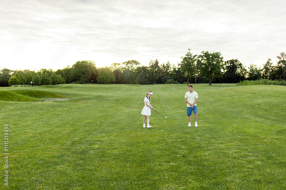 young sports couple in uniform playing golf together on field with lawn at sunset, woman with instructor practicing golf competitions and having active recreation young sports couple in uniform playing golf together on field with lawn at sunset, woman with instructor practicing golf competitions and having active recreation