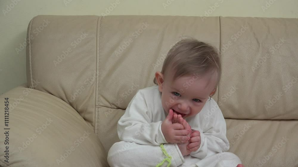 Cheerful baby on sofa tasting the foot toe and laugh Cheerful baby on sofa tasting the foot toe and laugh