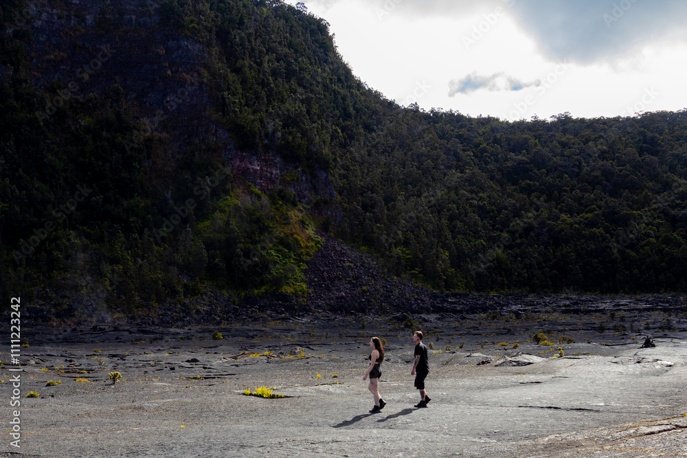 Man and woman walking across black barren landscape in Volcanos National Park in Big Island Hawaii Man and woman walking across black barren landscape in Volcanos National Park in Big Island Hawaii