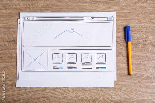 Developing UI design. Sketches of website wireframes and pen on wooden table, top view photo