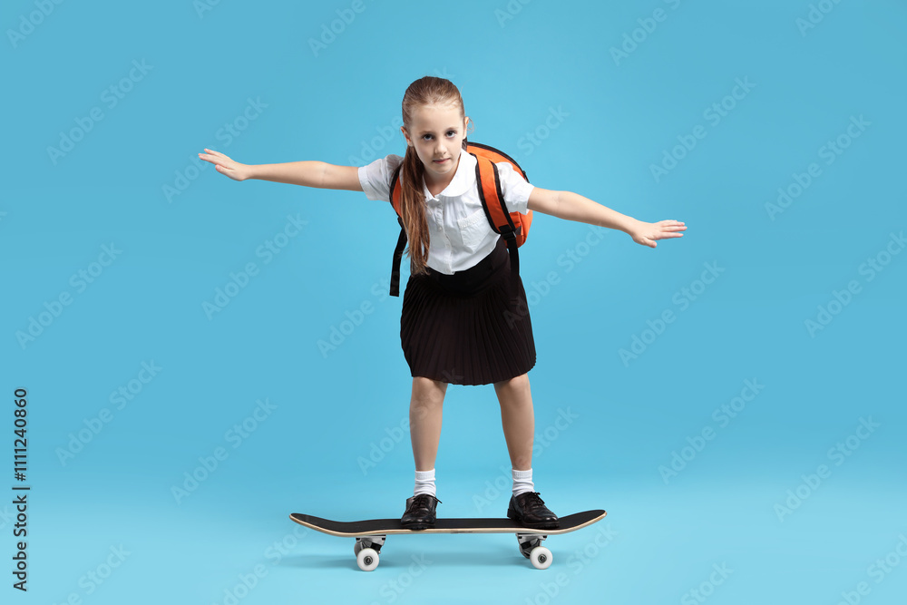Little girl standing on skateboard against light blue background