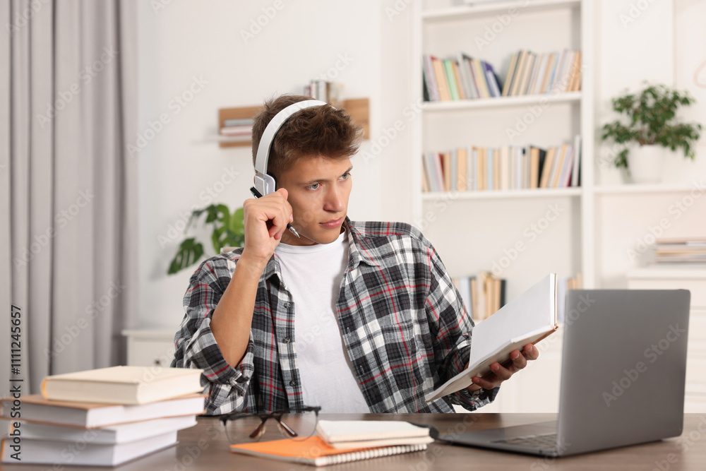 Student in headphones studying at table indoors Student in headphones studying at table indoors