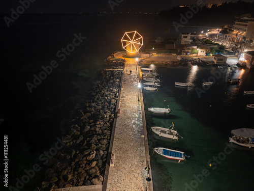 A large windmill with a lit up top is lit up at night. The windmill is surrounded by a stone walkway photo