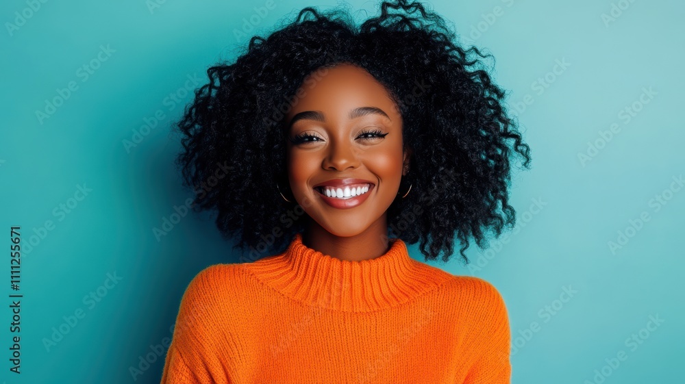 Happy young African American woman with curly hair wearing a bright orange sweater standing against a solid blue background Happy young African American woman with curly hair wearing a bright orange sweater standing against a solid blue background