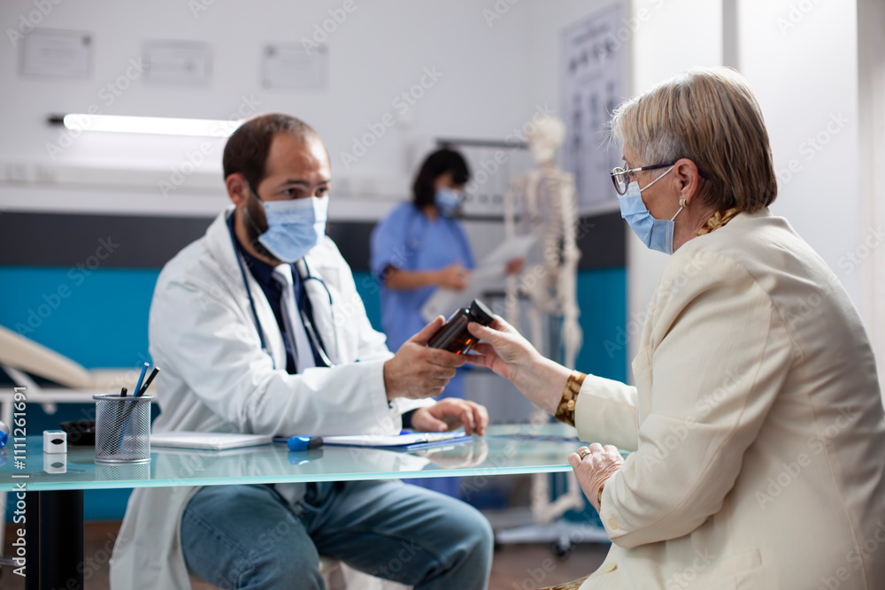 Obraz premium Caucasian old woman listens attentively as physician wearing stethoscope offers prescription pill bottle and explains drug effects during consultation. Pensioner patient receives medicine from doctor.