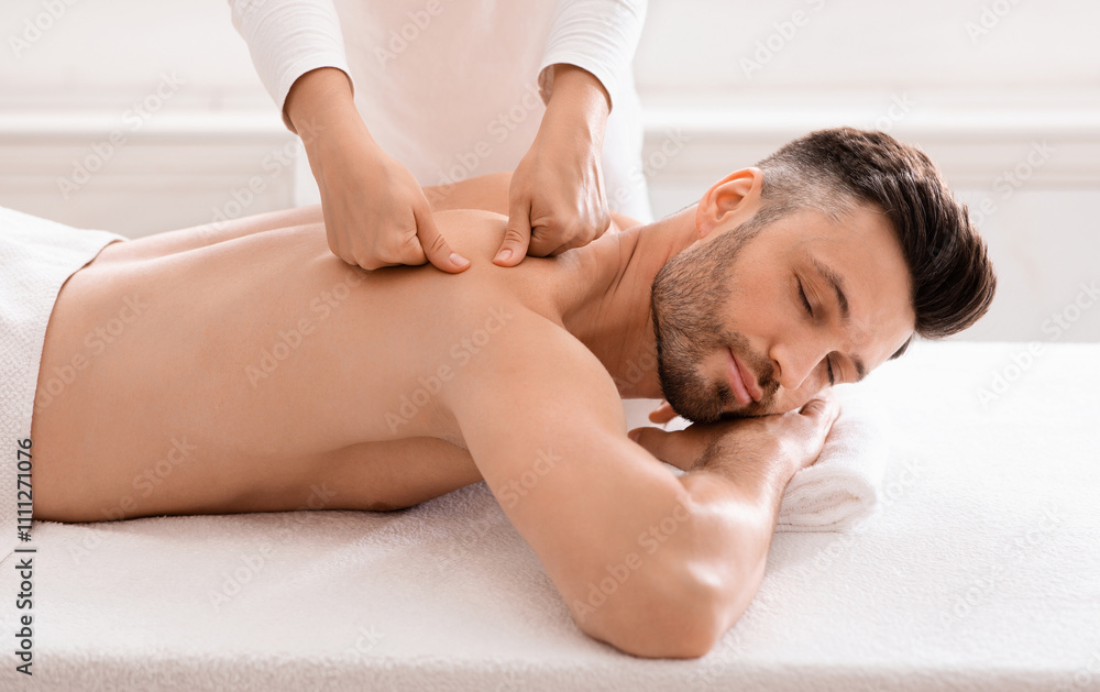 Middle aged bearded man attending modern male spa, laying on massage table, getting healing body procedure, enjoying his day at spa. Masseuse pressing on man back, using acupressure technique Middle aged bearded man attending modern male spa, laying on massage table, getting healing body procedure, enjoying his day at spa. Masseuse pressing on man back, using acupressure technique