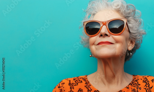 Happy smiling senior woman wearing sunglasses, teal blue solid colorful background, image with space for text