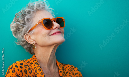 Happy smiling senior woman wearing sunglasses, teal blue solid colorful background, image with space for text