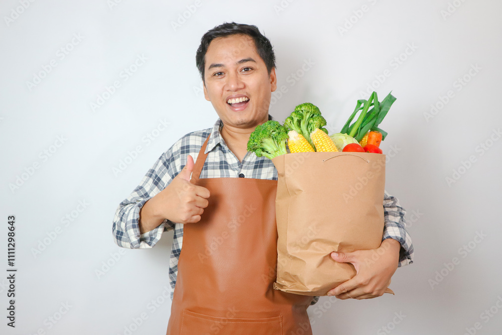 Asian man holding grocery shopping bag with vegetables with thumbs up gesture for healthy lifestyle concept Asian man holding grocery shopping bag with vegetables with thumbs up gesture for healthy lifestyle concept