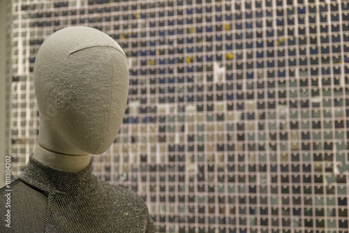 A mannequin with a fabric head stands in front of a glittering wall made of many small, shiny, square sequins