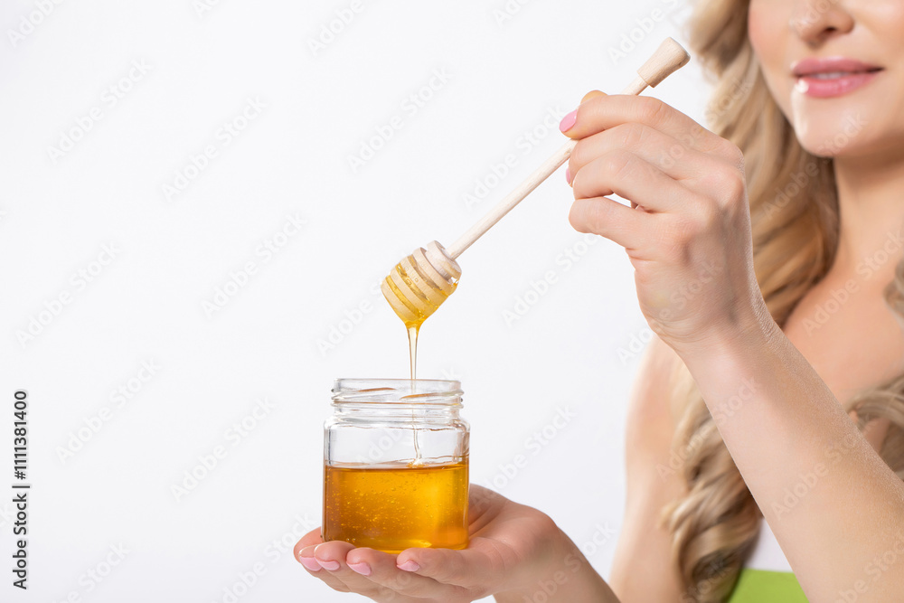 Fototapeta premium A Woman Carefully and Artfully Drizzling Golden Honey from a Jar Using a Dipper Tool