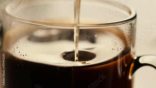 Freshly brewed coffee being poured into a transparent glass cup photo