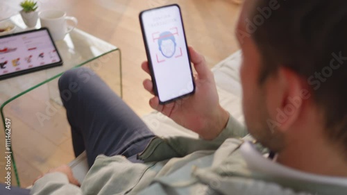 Man using face recognition on smartphone to confirm cashless transaction, over shoulder view. Online shopping and secure digital banking concept