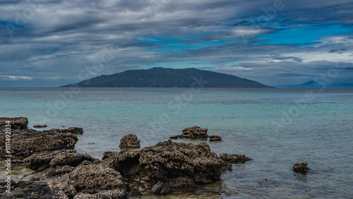 A calm seascape. Low tide time. Clams were attached to exposed boulders. Turquoise ocean. A hill on the horizon against a background of blue sky and clouds. Madagascar. Nosy Tanikeli    photo