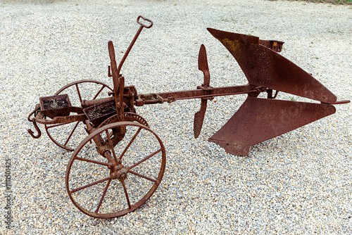 A vintage plow rests on a gravel surface, highlighting its rusted metal and unique design. The plow symbolizes traditional farming practices and agricultural history.