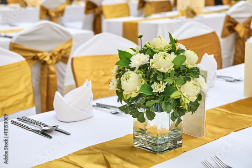 Elegant wedding reception table with floral centerpiece and gold decorations in a banquet hall setting. photo