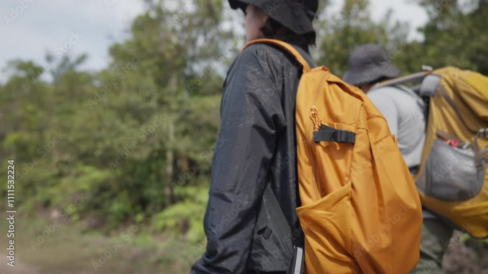 Two people are walking in the woods, one of them wearing a black jacket and the other wearing a yellow backpack Two people are walking in the woods, one of them wearing a black jacket and the other wearing a yellow backpack