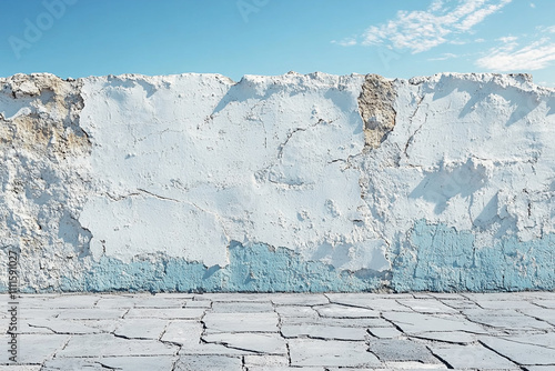 Weathered Wall and Cracked Pavement Under Blue Sky