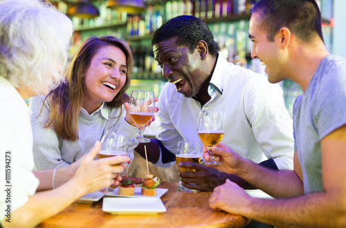 Spending time in bar. Four positive friends drinking beer in bar