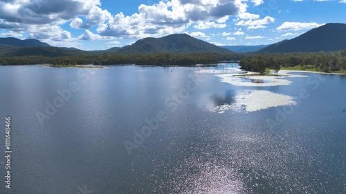 Aerial flies low over the sparkling surface of MacKay region's Lake Teemburra, past waterlogged tree trunks, mysterious inlets and mats of floating lilies under a dappled blue sky Australia photo