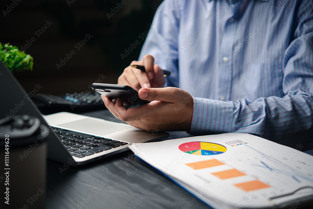 Fototapeta premium Businessman using mobile phone and computer to analyze financial accounting and marketing research data