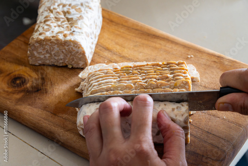 slicing thin raw tempeh block on a wooden board