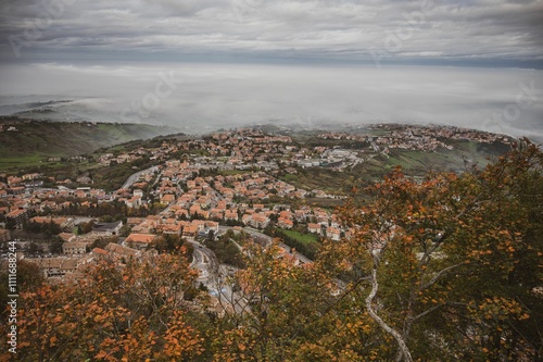 Aerial view of San Marino with autumn foliage and misty hills.