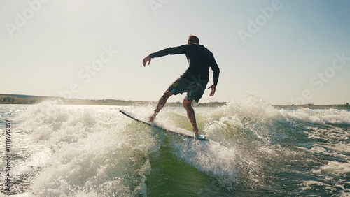 Wakeboarding behind a motorboat on the surface of the water. The scene conveys the dynamics, speed and adrenaline of water extreme sports. A man performs tricks while balancing on a wakeboard.