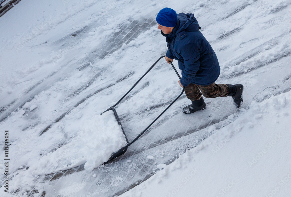 Fotografie A man in a blue jacket is pulling a snow plow