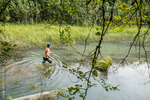 Shirtless man wading through wetland in lush forest photo