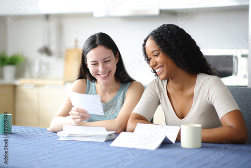 Happy interracial roommates or lesbian couple checking invoice photo