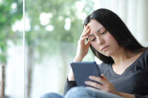 Worried asian woman reading ebook at home