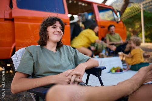 Smiling teenage boy sitting on chair with family in background at park photo